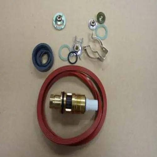Remeha Hydraulikbauteile, bestehend aus einer roten Schlauchleitung, einem Messingventil und mehreren Dichtungsringen sowie Metallclips, auf neutralem Hintergrund angeordnet.